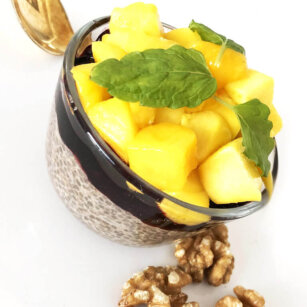 En skål med chiapudding med kokosmjölk toppad med mango och blåbär och valnötter vid sidan om.