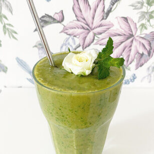 Ett glas selleri smoothie med banan och avokado toppad med en vit miniros.