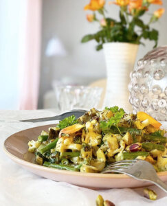 Ett fat med vegansk pytt i panna med trattkantareller med orangea blommor i bakgrunden.