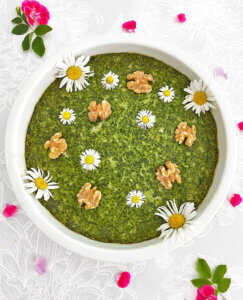 En vegansk och glutenfri spenatpaj med vegansk fetaost dekorerad med valnötter och blommor.