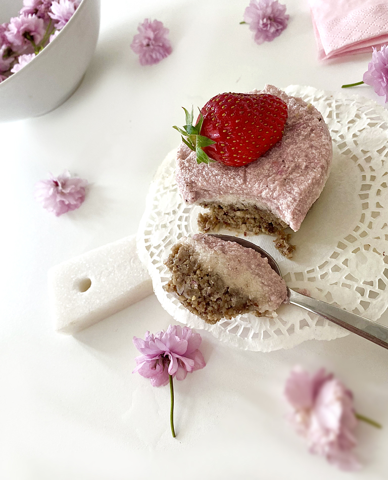 Cheesecake bakelser med jordgubbar - bakade på vita bönor ligger på ett fat med rosa blommor omkring.